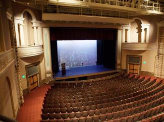 Large theatre with empty stage as viewed from the rear balcony of the house