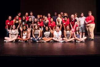 Photo of large group of college students, sitting and standing in rows, smiling, on a stage