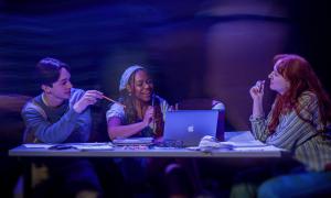 3 students sitting at a table while faded people walk around them
