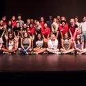 Photo of large group of college students, sitting and standing in rows, smiling, on a stage